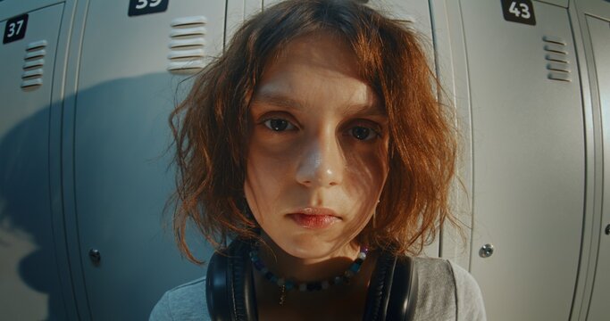 Portrait of Teenage Girl Wearing Headphones Looking Directly While Standing Near School Lockers Bathed in Warm Golden Hour Light. Confident Expression, Youth Culture, Modern Gen Z Student Lifestyle.