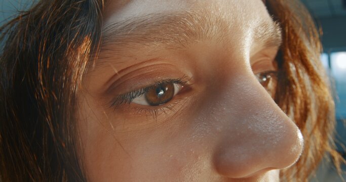 Close Up of Teenage Girl's Brown Eye and Face Illuminated by Warm Golden Sunset Light. Dreamy Cinematic Atmosphere, Natural Skin Texture, Quiet Contemplation. Youth, Introspection and Coming of Age.