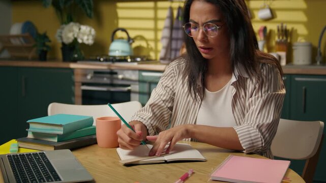 Stressed Latina high school girl studying at home writing homework frustrated student businesswoman freelancer multitasking with notebook difficult education problem distant learning busy at kitchen