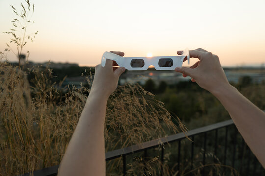 Hands holding solar eclipse glasses observing sun
