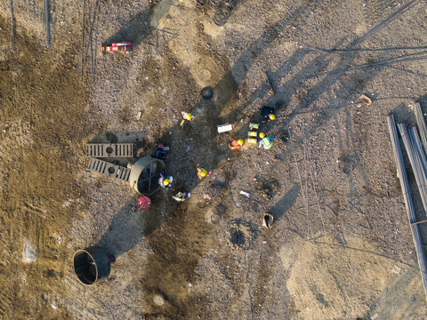 Aerial view of workers in hard hats at the Waste to Energy Facility Construction Project with construction materials on the dirt ground in Kecamatan Denpasar Selatan, Bali, Indonesia.