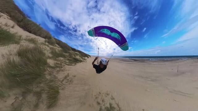Paraglider does thrilling coastal dune soaring over Dutch beach, rear POV