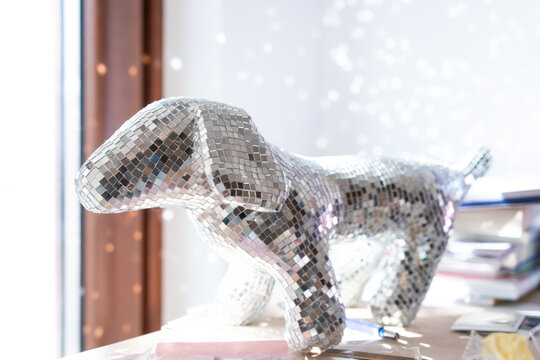 A decorative dachshund shaped object covered in tiny reflective mirror squares sits by a bright window, scattering points of light across the room, a festive party mood accent for the home.