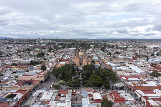 Aerial view of the Parroquia de Nuestra Senora de los Dolores in the town center, surrounded by colonial architecture, red-tiled roofs, and trees in Dolores Hidalgo, Guanajuato, Mexico.