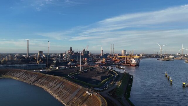 Drone approaches steelworks above harbor facilities with ships and stockpiles