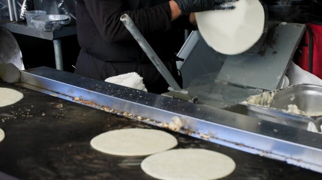 Traditional cooking footage showing lady in background making tortillas with flat grill in the foreground during preparation of fresh handmade corn tortillas
