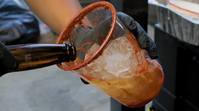 Beverage preparation footage showing man pouring beer into cup for michelada during preparation of a savory Mexican michelada drink