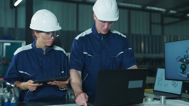 Industrial team examining technical blueprints and tablet in factory meeting