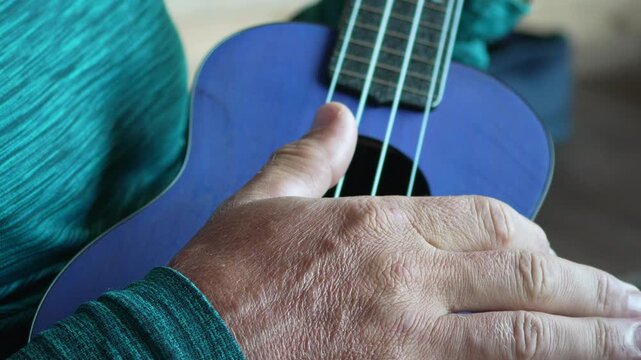 Ukulele playing music, close-up of hand strumming strings on a purple instrument.