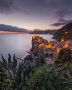 View of the historic coastal village of Vernazza at sunset, with illuminated stone buildings perched on the cliffs overlooking the Mediterranean Sea, Vernazza, Liguria, Italy.