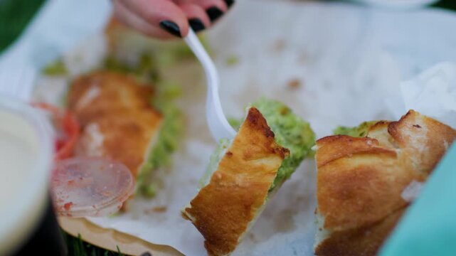 A young woman eats pide at a cozy street food festival, sampling various street foods. Close-up of the food. Summer vibes.