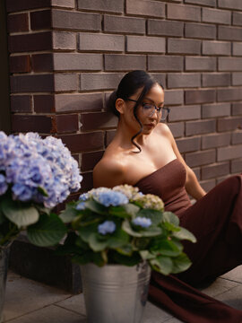 Asian Woman Leaning Brick Wall Near Blue Hydrangeas Outdoors