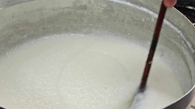 Cooking white rice porridge in metal pot.