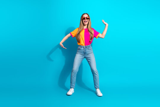 Young stylish woman dancing in bright pink orange top jeans and white sneakers against blue background