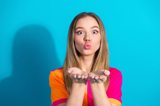 Young woman blowing kiss at camera against blue background wearing bright pink and orange shirt