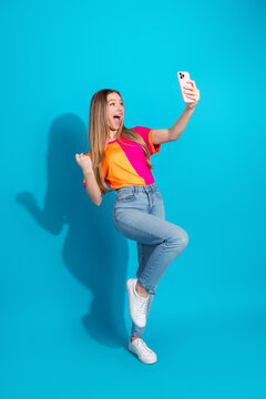 Young woman takes a joyful selfie in a vibrant shirt against a blue background