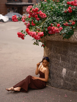 Asian Woman Sitting Near Stone Wall Under Blooming Roses