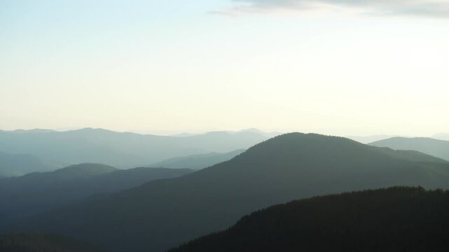 Mountain landscape with silhouettes of peaks in soft sun rays, green and blue tones
