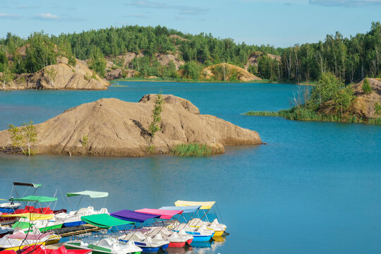 High angle view of variety of colorful boats moored at a tranquil lake with green hills and clear blue water in the background in Konduki, Tula region, Russia.