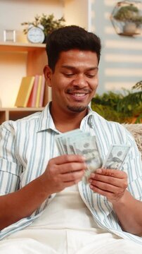 Indian man on home sofa counts cash with pleased mood and thinks about spending plans and savings at home. Arabian boy on home sofa checks banknotes and calmly plans budget for future goals and needs.