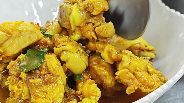 Pouring yellow curry sauce over chicken meat.