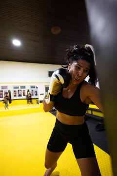 Determined Female Boxer Training Intense Punches On Heavy Bag In Bright Gym Session
