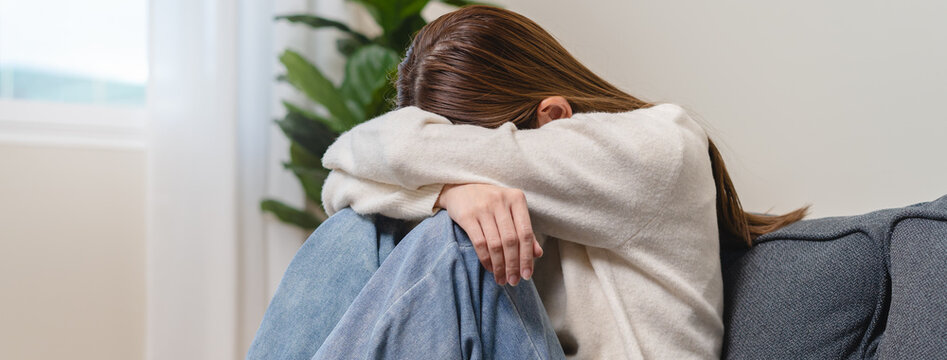 Anxiety young woman sitting on sofa covering her face at home.