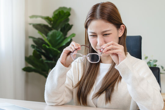 Eye problem concept, fatigue asian young woman tired eyes, irritated rubbing eye dry relief vision pain after work on laptop computer, eye strain, hand holding glasses, suffer migraine, bad blurry