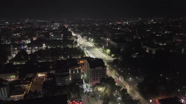 Cinematic drone pullback revealing central Chisinau, Moldova at night, with the illuminated main boulevard, moving traffic, Cathedral Park, city buildings and the urban skyline stretching into the dis