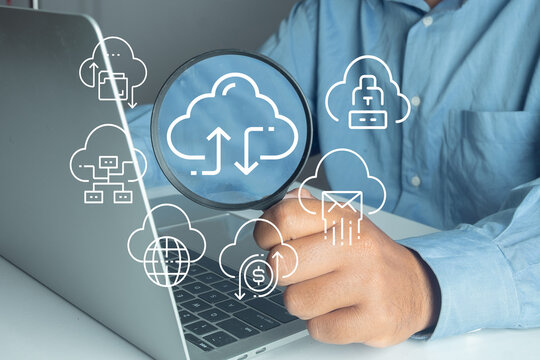 A businessman holding a magnifying glass over a laptop with digital cloud computing and data storage icons overlay. Concept of cloud technology, data synchronization, and digital transformation.
