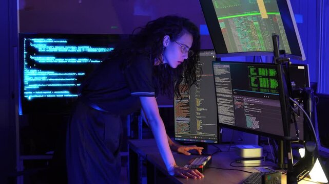 Female software developer working with multiple monitors display programming code in a modern technology workspace. coding, cybersecurity, digital technology, data processing, programming, innovation.