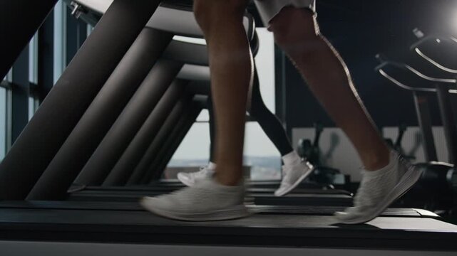 Close up male legs running on treadmill in fitness gym sports shoes unrecognizable guy runner jogging run machine sporty couple training cardio workout woman man athletic feet stride exercise indoor