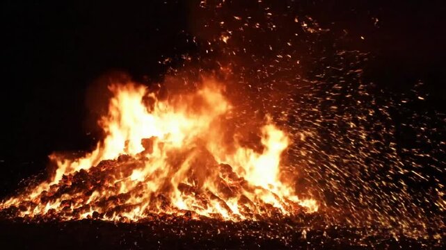 Large bonfire ablaze at night with sparks flying into the darkness during a festive celebration