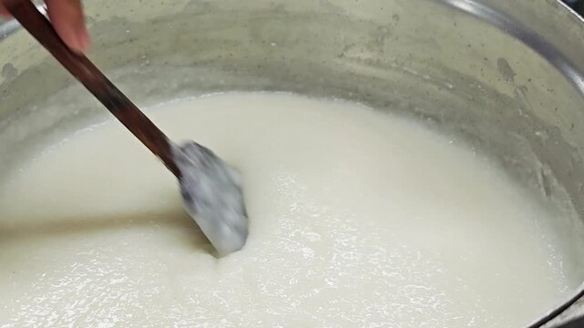 Pouring creamy white congee into cooking pot.