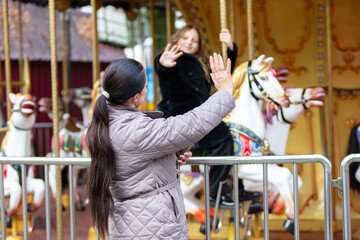 Woman waving at a child on a carousel ride with horses in an amusement park © Светлана Лазаренко