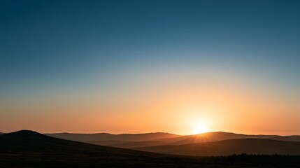 Fototapeta premium Vibrant sunset over rolling hills landscape with gradient sky and silhouetted mountains