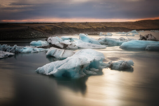 View of icebergs floating in the calm waters of the Jokulsarlon Glacier Lagoon during golden hour in Hornafjordur, Iceland.