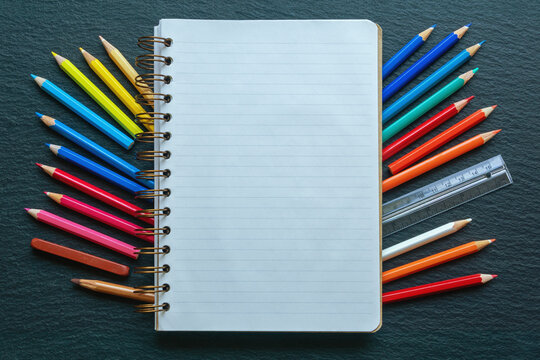 Spiral notebook and colored pencils on a black table. Copy space