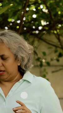 Indian Asian mid age couple in their fifties walking in the park, smiling and pointing, enjoying a pleasant conversation on a sunny day outdoors