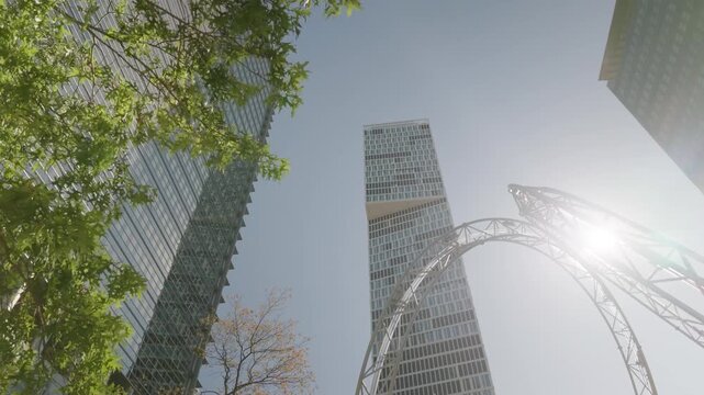 Germany Frankfurt am Main low angle view of glass skyscrapers with steel arch and green trees