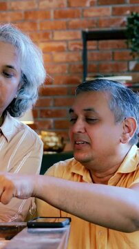 Indian Asian mid age couple in their fifties with gray hair playing carrom, enjoying an indoor board game with a light and happy mood