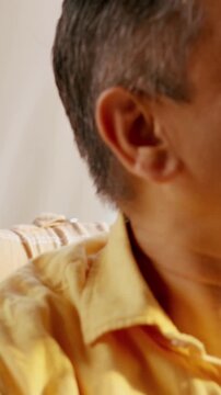Indian Asian couple in their fifties with gray hair enjoying tea or coffee by a sunny window, relaxing on the sofa and spending quality time together in the morning