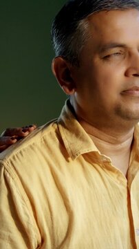 Indian Asian couple in their fifties with grey hair standing close by a large window, bathed in morning sunlight, both gazing outside with serious expressions, reflecting in the moment