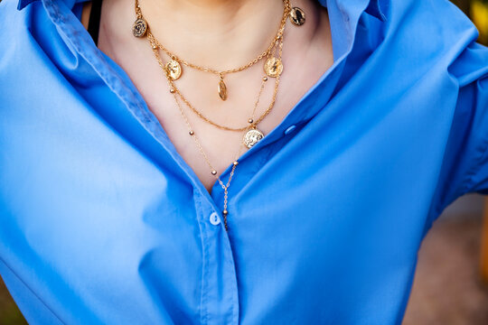 Close up of woman in bright blue button down shirt and elegant layered gold coin necklace. Modern feminine fashion and stylish jewelry detail.