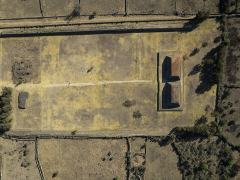 Aerial view of the Zona Arqueologica de Ihuatzio, featuring ancient stone pyramids and a large open plaza surrounded by dry fields and stone walls in Ihuatzio, Michoacan, Mexico.