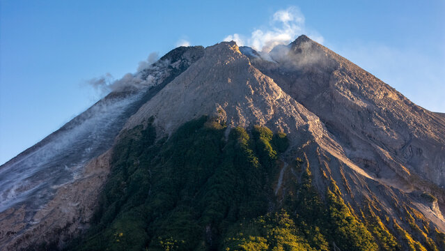 Aerial view of Mount Merapi, an active volcano with smoke rising from its crater, rocky slopes, and lush green vegetation in Yogyakarta, Special Region of Yogyakarta, Indonesia.