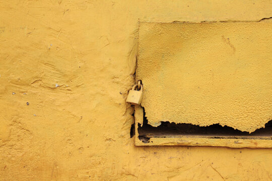 Abstract close-up of a yellow padlock attached to an aged yellow wooden surface