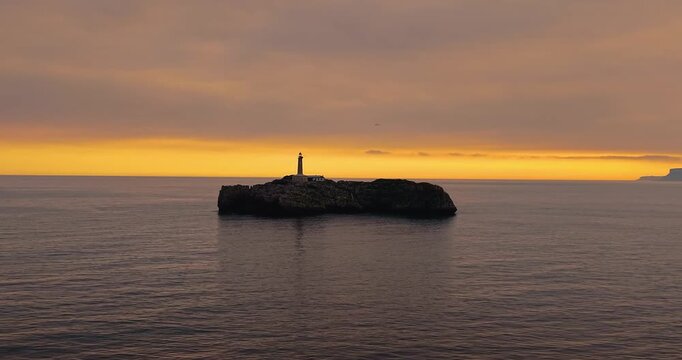 Cinematic aerial view of Mouro Island (Isla de Mouro) lighthouse at dramatic sunset in Santander bay, Cantabria, Northern Spain.