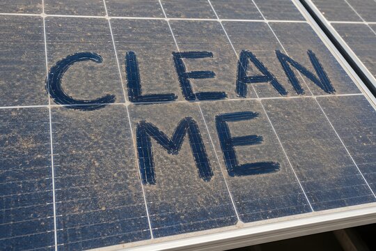 Clean me text written on a dusty solar panel surface