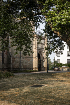 View of the historic stone entrance of Worcester Cathedral framed by a large tree in the foreground in Worcester, England, United Kingdom.